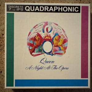 May include: A square album cover for Queen's "A Night At The Opera" features the band's crest in the center, with a white background and colorful accents. The top of the cover reads "QUADRAPHONIC". The album title and band name are in elegant script.