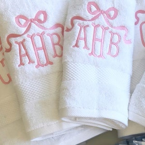 May include: Three white towels with pink embroidered bows and the letters "AHB" on each towel.