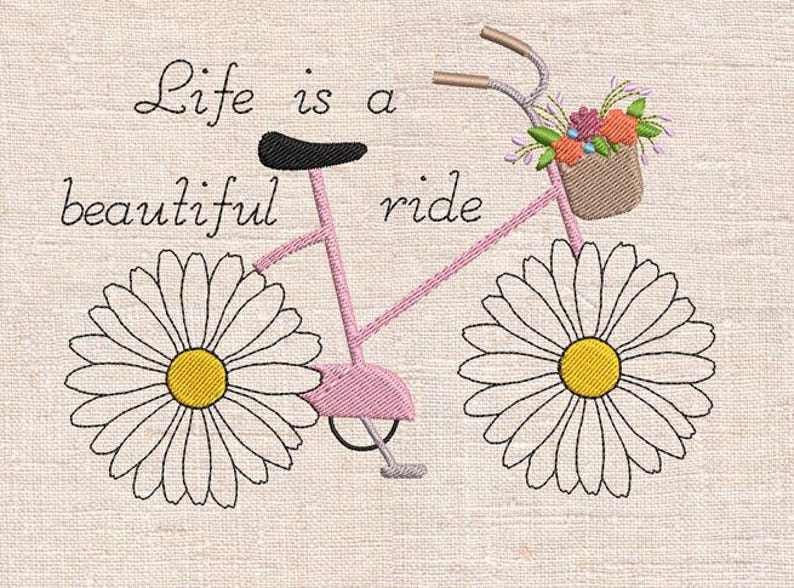 Op de afbeelding: Geborduurd beeld van een roze fiets met madeliefjeswielen en een bloemenmand. De tekst "Life is a beautiful ride" is boven de fiets geborduurd. De achtergrond is een lichtbeige stof.