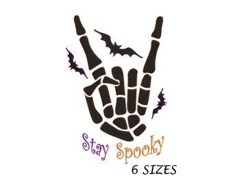 May include: Black skeleton hand making a rock and roll hand gesture with bats flying around it. The text "Stay Spooky" is below the hand in orange and purple lettering. The text "6 SIZES" is below the text "Stay Spooky" in purple lettering.