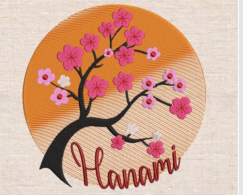 May include: Embroidered design of a pink cherry blossom tree with a sunset background and the word "Hanami" in red lettering.