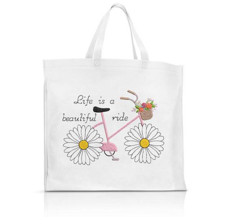Op de afbeelding: Witte draagtas met een roze fietsontwerp, madeliefjeswielen en een bloemenmand. De tekst "Life is a beautiful ride" staat op de tas. Het heeft twee witte handvatten.