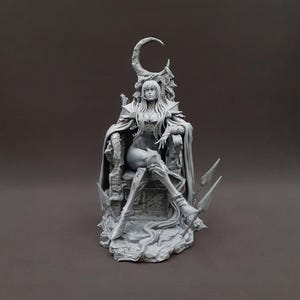 May include: A grey figurine of a woman seated on an ornate throne. The figure wears a cape and high boots, with a crescent moon design above her head. The throne is detailed with intricate carvings and the figure has long flowing hair.