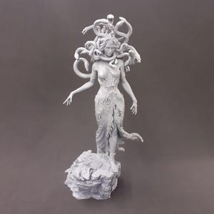 May include: A gray, 3D printed statue of Medusa, the Greek mythological figure with snakes for hair. She is standing on a rocky base and has a fierce expression on her face.