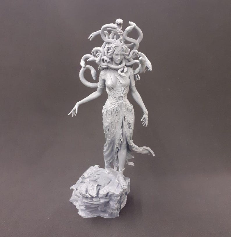 May include: A gray, 3D printed statue of Medusa, the Greek mythological figure with snakes for hair. She is standing on a rocky base and has a fierce expression on her face.