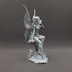 Puede incluir: Figura de hada gris con grandes alas detalladas y una delicada corona. El hada está sentada en una rama de árbol, con intrincados detalles en la escultura. La figura tiene una expresión serena y es un objeto decorativo de temática fantástica.