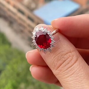 Peut inclure: Une bague en argent avec une grande pierre de rubis ovale entourée d'un halo de petits diamants.