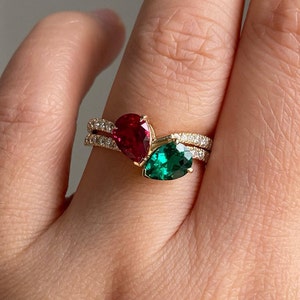 May include: A gold ring with two pear-shaped gemstones. The larger gemstone is a vibrant green, and the smaller gemstone is a deep red.