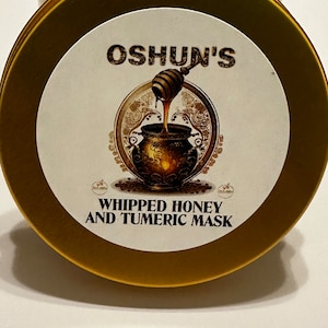 Könnte beinhalten: Goldener Deckel mit einem weißen Etikett, auf dem "OSHUN'S" in schwarzer Schrift steht. Das Etikett zeigt auch eine Zeichnung eines goldenen Topfes, in den Honig gegossen wird. Der Text "WHIPPED HONEY AND TUMERIC MASK" befindet sich unterhalb der Zeichnung.