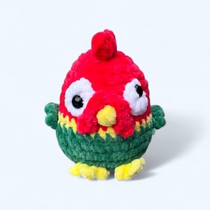 May include: A crocheted plush toy shaped like a bird with a red head, green body, and yellow feet. The bird has large white eyes with black pupils.