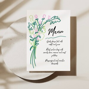 May include: A white menu card with a green and pink floral illustration. The menu lists: Goats cheese tart with rocket and pear, Roast sirloin beef with carrots, bone marrow and roast potatoes, Passionfruit and vanilla cheesecake.