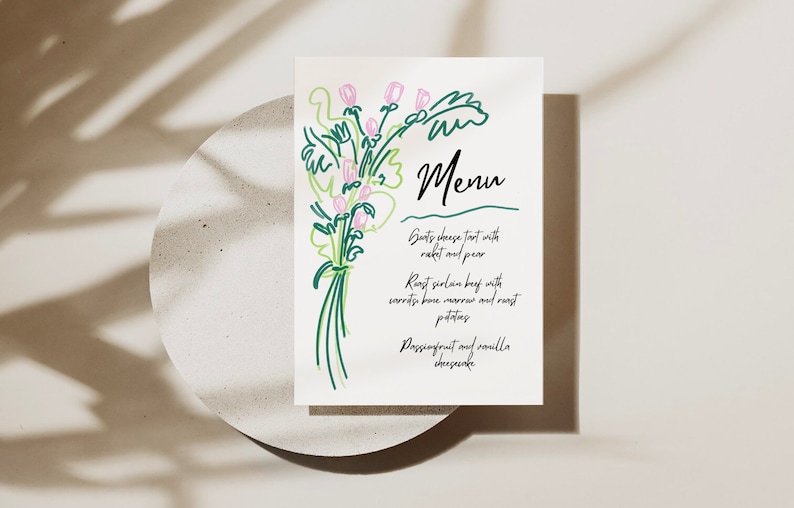 May include: A white menu card with a green and pink floral illustration. The menu lists: Goats cheese tart with rocket and pear, Roast sirloin beef with carrots, bone marrow and roast potatoes, Passionfruit and vanilla cheesecake.