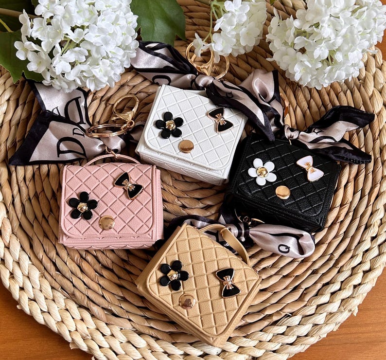 May include: Four small quilted purses with a bow and flower embellishment. Each purse has a gold key ring attached. The purses are in pink, white, black, and beige.