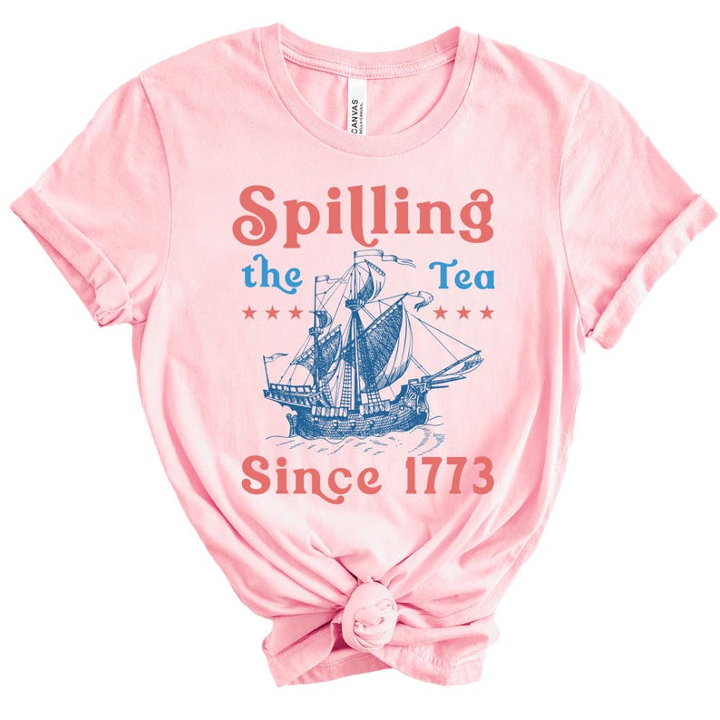 May include: A pale pink t-shirt with the words "Spilling the Tea Since 1773" in red and blue. A blue illustration of a sailing ship is centered on the shirt, with stars on either side.