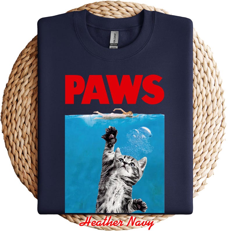 K&ouml;nnte beinhalten: Marineblaues Sweatshirt mit einem Parodie-Design. Das Design zeigt das Wort "PAWS" in Rot, eine Katze, die aus dem Wasser greift, und einen Schwimmer. Der Text "Heather Navy" befindet sich unten.