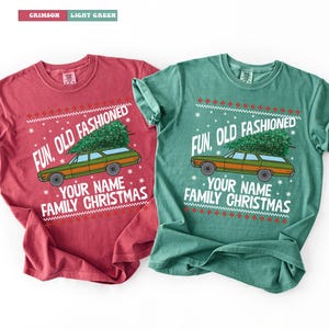 May include: Two t-shirts, one crimson and one light green, display a Christmas-themed design. The design includes a station wagon with a Christmas tree, the text "FUN, OLD FASHIONED", and space for a name and "FAMILY CHRISTMAS".