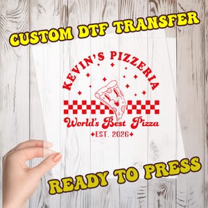 May include: Clear DTF transfer sheet with a red "Kevin's Pizzeria" logo, a pizza slice graphic, and the text "World's Best Pizza" and "EST. 2026". The words "CUSTOM DTF TRANSFER" and "READY TO PRESS" are in yellow.