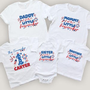 May include: A collection of white t-shirts and a onesie with patriotic designs. The shirts read "Daddy," "Mommy," "Brother," and "Sister" of the "Little Firecracker." One shirt says "This Firecracker is 1 Carter."