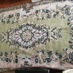 Könnte beinhalten: Ein Vintage-Teppich mit einem floralen Muster in Rosa-, Grün- und Brauntönen. Der Teppich hat ein zentrales Medaillon mit einem aufwendigeren Design.