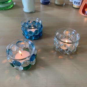 Puede incluir: Tres portavelas de vidrio con velas de té. Los portavelas están decorados con cuentas de vidrio azul y verde.
