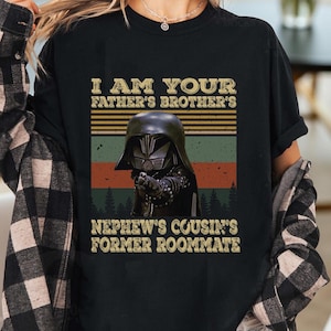 May include: Black t-shirt featuring a graphic of Darth Vader with the text "I AM YOUR FATHER'S BROTHER'S NEPHEW'S COUSIN'S FORMER ROOMMATE". The design has a vintage, retro style with a color block background.