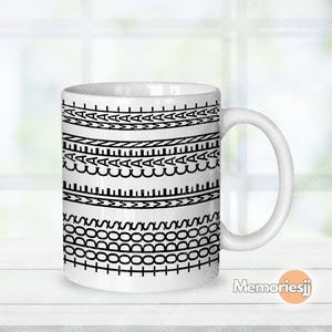 以下が含まれることがあります： 白のセラミックコーヒーマグ。黒の幾何学模様が並んでいます。模様には線、三角形、円が含まれます。マグには白いハンドルがあり、背景はぼやけています。