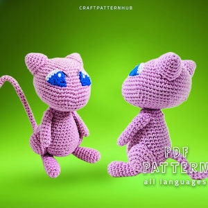 May include: A pink crocheted amigurumi toy of a cat-like Pokemon character with blue eyes. The toy is sitting on a green background. The text "PDF PATTERN all languages" is visible in the image.