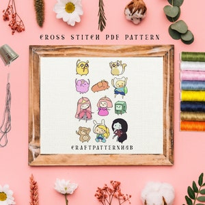 Op de afbeelding: Een kruissteekpatroon met personages uit de animatieserie Adventure Time. Het patroon bevat Finn, Jake, Prinses Bubblegum, Marceline en andere personages. Het patroon is in een houten frame en klaar om te worden gestikt.