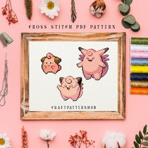 Könnte beinhalten: Kreuzstichmuster mit drei rosa Pokémon-Charakteren, darunter ein Jigglypuff, ein Wigglytuff und ein Clefairy. Das Muster ist in einem Holzrahmen gerahmt und auf einem rosa Hintergrund dargestellt. Der Text "CROSS STITCH PDF PATTERN" befindet sich oben am Rahmen und "CRAFTPATTERNHUB" unten am Rahmen.