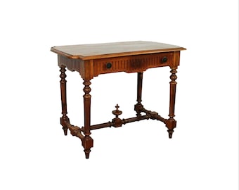 May include: A vintage wooden side table with a rectangular top and a single drawer. The table features ornate, turned legs and decorative crossbars. The wood has a warm, medium-brown tone, and the drawer has a dark knob.