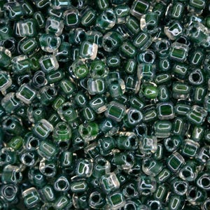 Peut inclure: Gros plan sur un tas de petites perles carrées. Les perles sont d'une couleur vert d'eau translucide avec un carré vert foncé au centre. Les perles sont éparpillées, créant une surface texturée.