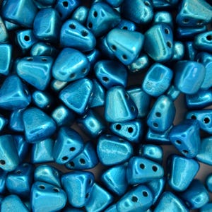 May include: A close-up of a pile of turquoise blue triangle-shaped beads. The beads have a metallic sheen and are made of glass.