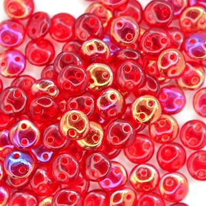 May include: A pile of small, round, red glass beads with iridescent gold and purple accents. The beads have two holes each.