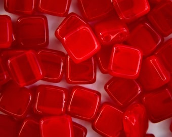 May include: A close-up of a group of red glass square tiles. The tiles are scattered on a white surface.