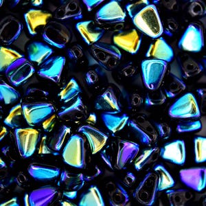 May include: A close-up of a pile of iridescent blue and gold triangle-shaped beads. The beads have a metallic finish and are perfect for jewelry making.