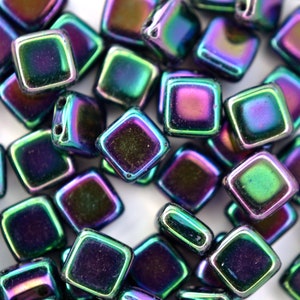 May include: A close-up of a pile of iridescent square glass beads. The beads are a mix of purple, green, and blue.