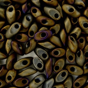 Könnte beinhalten: Nahaufnahme eines Haufens kleiner, brauner, irisierender Glasperlen. Die Perlen sind oval geformt mit einem Loch in der Mitte.
