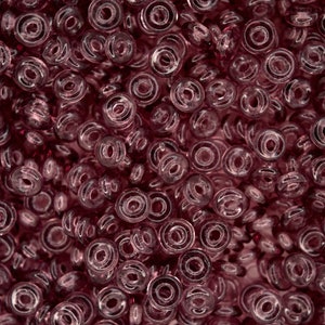 May include: A close-up image of a large quantity of small, round, translucent, burgundy-coloured beads with a white ring around the centre of each bead.