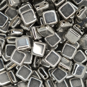 May include: A close-up of a pile of silver-coloured square beads. The beads are shiny and have a slightly textured surface.