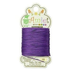 May include: A spool of vibrant purple Amiet polyester thread, ideal for crafting. The label features the brand name, Japanese text, and floral illustrations. The spool contains 20 meters of thread, perfect for various sewing projects.