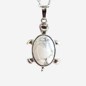 May include: A silver-toned turtle pendant necklace. The pendant features a white oval stone with gray veining, set in a turtle-shaped frame. The necklace has a delicate chain and a simple clasp.