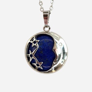 May include: Silver pendant necklace with a round pendant. The pendant has a dark blue stone centre, a crescent moon design, and cut-out stars. A small gem is set on the moon's face. The necklace chain is silver.