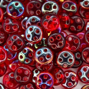 May include: A close-up of a pile of red glass beads, each with four holes. The beads have an iridescent finish.