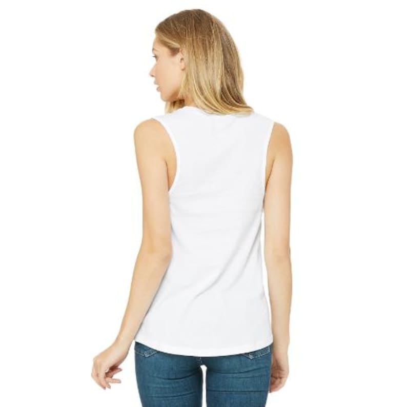May include: A white sleeveless tank top made of a soft material. The tank top is shown from the back, with a woman wearing it and blue jeans. The tank top has a scoop neck and a relaxed fit.
