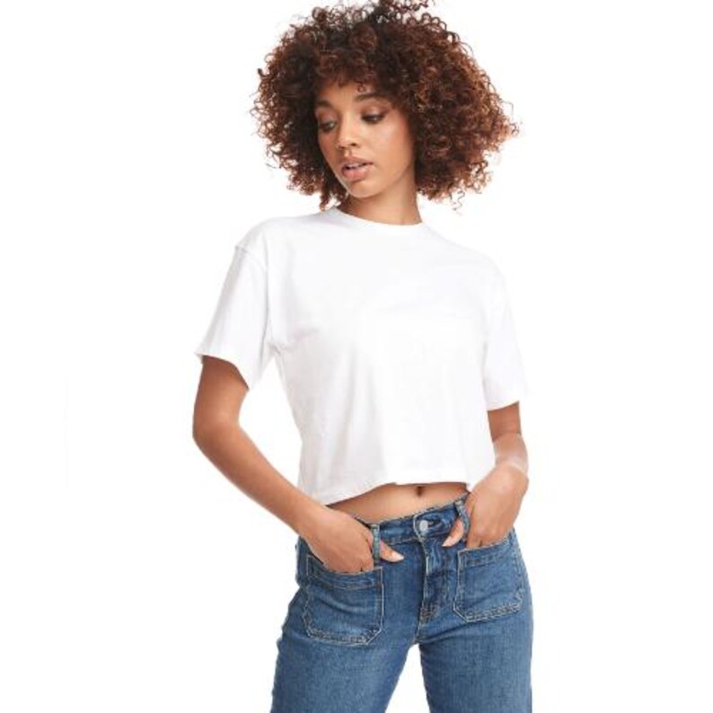 May include: A white, cropped t-shirt with short sleeves. The model is wearing blue denim jeans with pockets. The background is plain white.