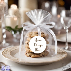May include: A stack of chocolate chip cookies in a clear cellophane bag tied with a white ribbon. The bag has a white circle sticker with the text "Your Design Here".