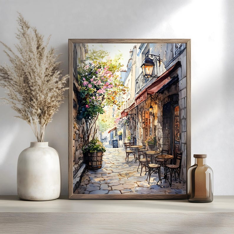 May include: A watercolor painting of a Parisian street scene with a cafe on the corner. The cafe has red awnings and a stone facade. There are tables and chairs set up outside the cafe, and people are sitting and enjoying the atmosphere. The street is cobblestone and lined with buildings. There are trees and flowers in the background.