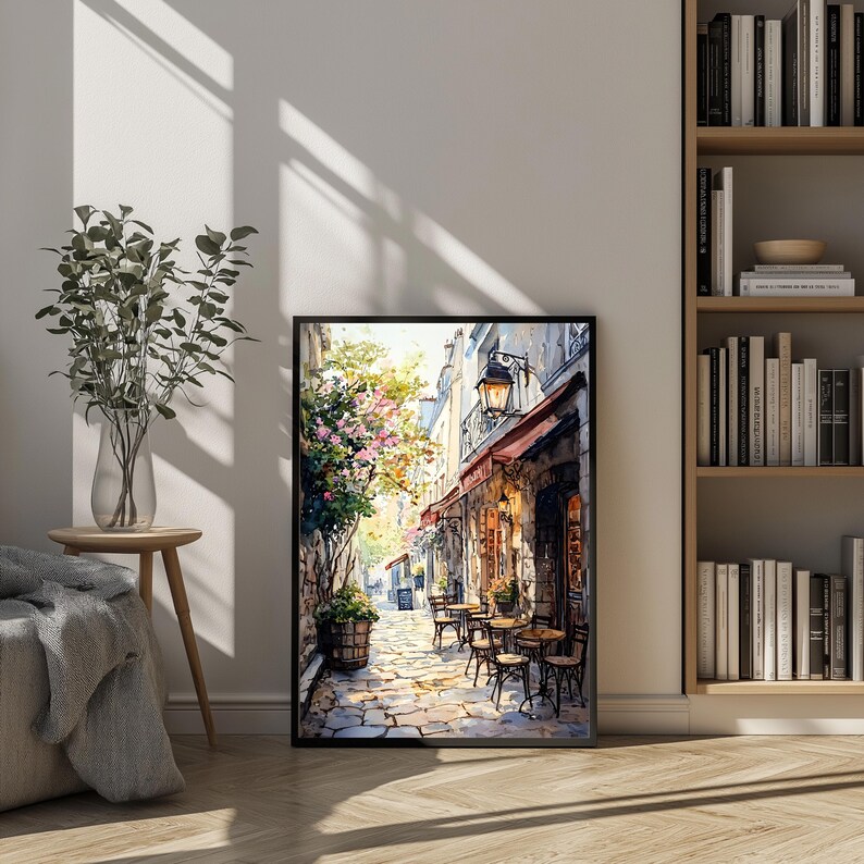 May include: A watercolor painting of a narrow street in a European city. The street is lined with buildings, and there are trees and flowers growing along the sides. There are tables and chairs set up outside a cafe, and people are sitting at the tables. The painting is done in a realistic style, and the colors are bright and vibrant.