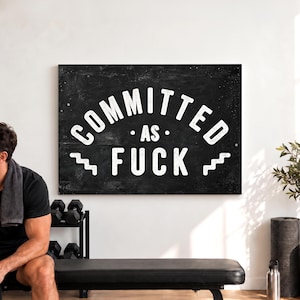 May include: A rectangular wall art piece featuring a black, distressed chalkboard-style background with white, bold, sans-serif text that reads COMMITTED AS FUCK, flanked by two small, white, zigzagging line graphics on either side of the word FUCK.