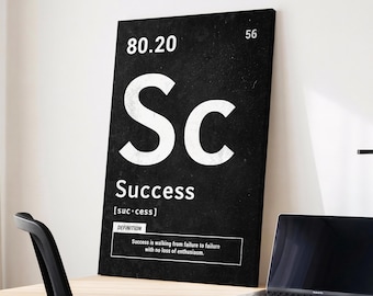 May include: Black and white wall art with the word "Success" in large white letters, styled like a periodic table element. The art includes the definition of success and sits on a wooden desk next to a laptop.
